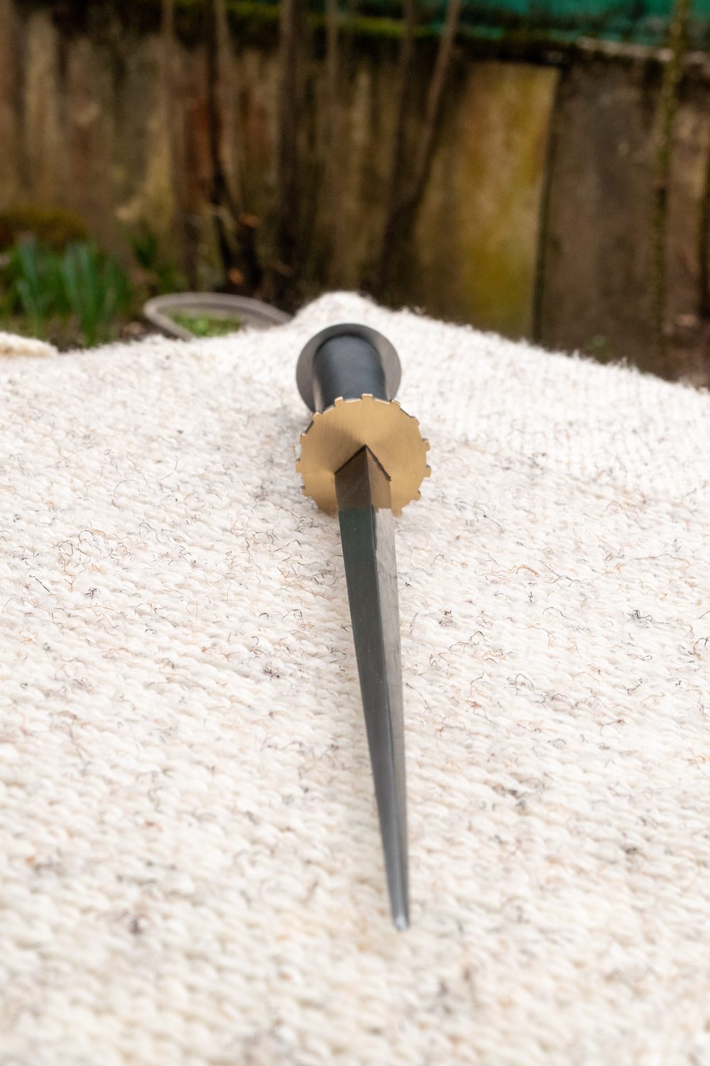 Rondel dagger with triangular blade and brass pommel, resting on cream fabric