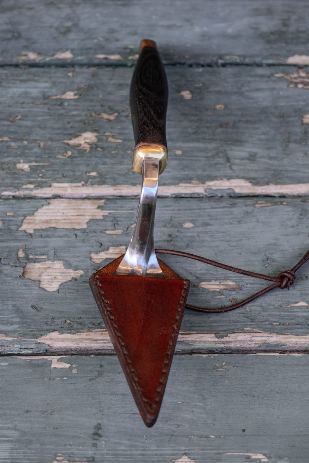 Hand-forged archaeologist's trowel with its leather sheath, resting on weathered painted wood