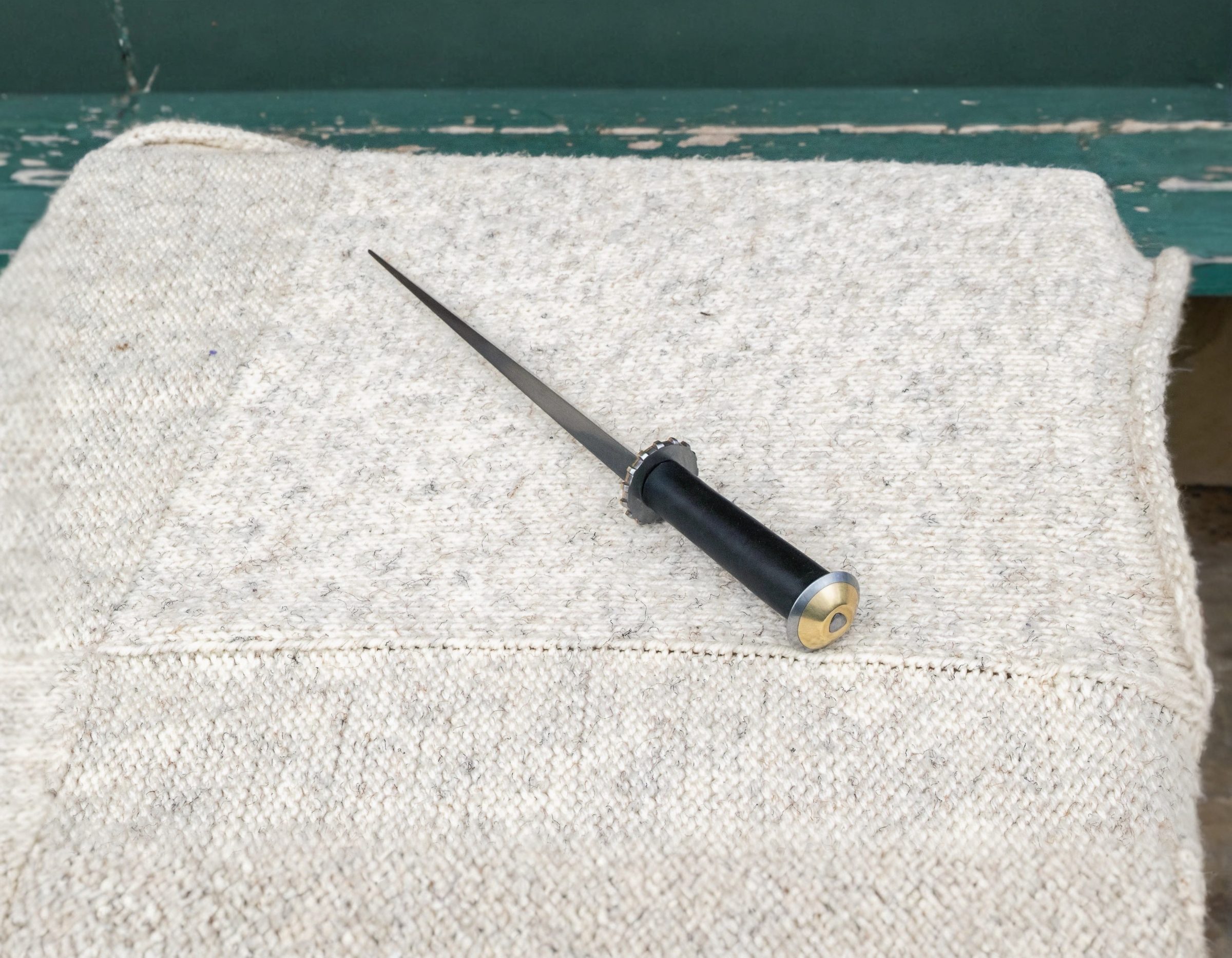 Rondel dagger with triangular blade and brass pommel, resting on cream fabric